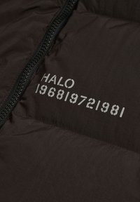 Czarna tkanina z zamkiem błyskawicznym i białym napisem w stylu szablonowym „HALO 196819721981” nadrukowanym blisko szwu zamka.