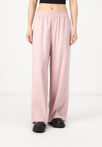 Světle růžové kalhoty širokého střihu z hladké tkaniny mají elastický pas a boční rozparky, v kombinaci s černými masivními botami.