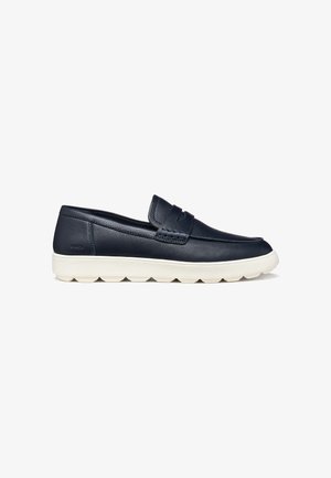 Mocassino slip-on in pelle nera con suola in gomma bianca, punta arrotondata e cinturino decorativo sulla tomaia.