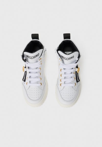 White high-top sneakers with a smooth leather finish, perforated detail, gold eyelets, and black accents, featuring a logo on the tongue.
