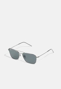 Sunglasses with gray lenses, a slim silver metal frame, angular design, and clear nose pads; arms tapering towards the ends.