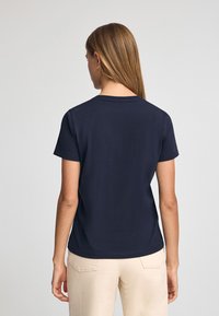 Mörkblå kortärmad t-shirt med rund halsringning och en slät textur, kombinerad med ljusa byxor. Enkel och klassisk design.