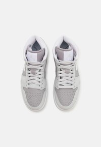 Tênis altos brancos e cinza, feitos com materiais de couro e malha, apresentam atacadores redondos, caixa do dedo perfurada e logotipo Jordan na língua.