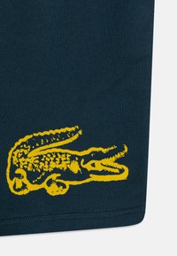 T-shirt en coton bleu foncé arborant un graphique d'alligator jaune vif, avec des détails fins sur les écailles et la texture le long des bords du design.