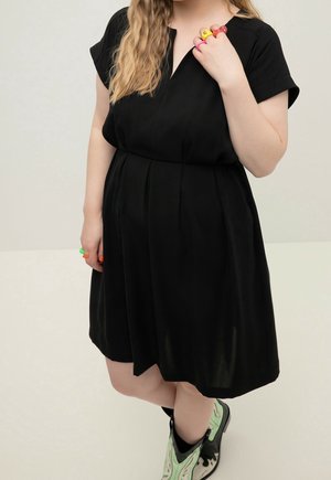 Femme en robe noire portant des bagues épaisses colorées et des bottes de cow-boy vert clair, avec des cheveux blonds ondulés visibles.