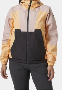 Färgglad huva-jacka med en design i gult och svart färgblock. Tillverkad av lätt och vattenavvisande material med elastiska ärmslut och dragkedjestängning.