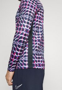 Dlouhý rukáv sportovního trička v navy barvě, s geometrickým růžovým a bílým vzorem. Texturovaný boční panel v černé barvě, úzký střih.