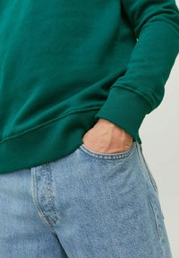Felpa verde in cotone con collo rotondo, polsini a coste e vestibilità rilassata, abbinata a jeans in denim blu chiaro.