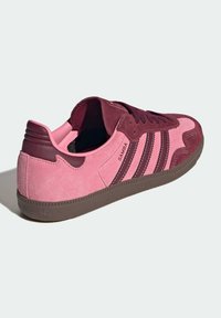 Sneakers aus Wildleder in Kastanienbraun und Pink mit drei dunklen Streifen, strukturierten Paneelen, einer Gummisohle und einem Logo an der Seite. Abgerundetes Zehendesign.