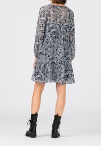 Pitkähihainen, harmaa ja musta paisley-kuvioinen mekko, jossa on kerroksellinen muotoilu, yhdistettynä mustiin nauhakiinnitteisiin nilkkureihin. Puolisiirtävä kangas.