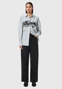 Koszula na guziki w paski w jasnoniebieskim i białym kolorze, z czarnym nadrukowanym logo. Połączona z czarnymi, szerokimi spodniami z wysokim stanem i butami na obcasie.