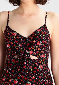 Svart blommig klänning med röda, rosa och gula blommor. V-ringning, justerbara axelremmar, knutdetalj fram och sidoutskärningar.