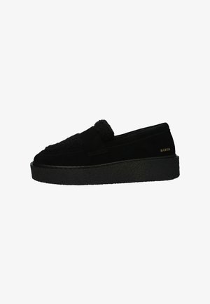 Schwarzer Slipper mit dickem strukturiertem Plattformsohle, Wildleder- und flauschigem Obermaterial sowie kleinem goldenen "BLOXSTN"-Logo in der Nähe der Ferse.