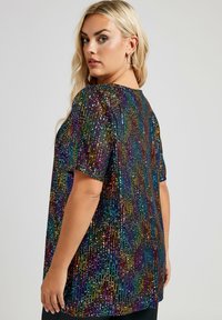 Blusa de lentejuelas con corte holgado, mangas cortas y patrones verticales multicolores en tonos púrpura, verde, azul y dorado.