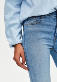 Vaqueros de denim azul claro con un corte ajustado, que presentan una sutíl textura desvaída, costuras en contraste y un bolsillo en el lateral.