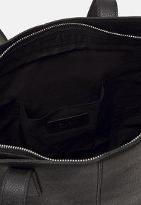 Borsa in pelle nera con chiusura a zip. L'interno è foderato in tessuto nero e presenta una tasca laterale con etichetta del logo. Texture liscia.