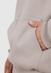 Hellgrauer Sweatshirt mit Kängurutasche und gerippten Bündchen. Weicher Stoff mit glatter Textur und minimaler Nähdetails.