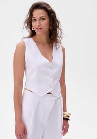 Biały lniany bezrękawnik z dekoltem w kształcie litery V, z pięcioma guzikami i krojem krótkim. Gładka tekstura i dopasowany krój, w połączeniu z pasującymi spodniami.