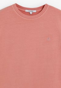 Koszulka z krótkim rękawem w zblakłym koralowym kolorze, wykonana z miękkiego materiału, z okrągłym dekoltem i małym wyszywanym logo na piersi.