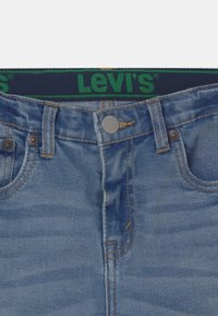 Ljust blå denimjeans med en Levi's midja, med kopparfärgade knappar, synlig sömnad och en lätt slitna textur.
