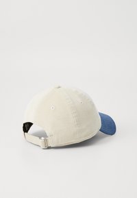 Kappe med en kremfarget cordfløyelsøke og en blå cordfløyelsvisir. Justerbar metallstropp bak, seks ventilasjonsøyler på toppen.