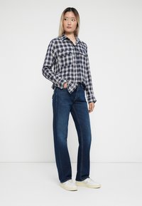 Marineblå og hvit rutete skjorte med knappestolpe, to brystlommer, kombinert med mørkeblå rette jeans og hvite sneakers.