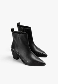 Botas de tobillo de cuero negro con punta afilada, cierre de cremallera y tacón cuadrado. Presenta tachuelas a lo largo de la suela para un detalle adicional.