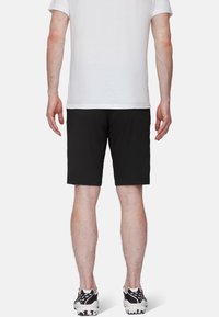 Pantalones cortos negros hechos de tejido ligero, con un diseño sencillo, dobladillo a la altura de la rodilla y combinados con zapatillas deportivas blancas.