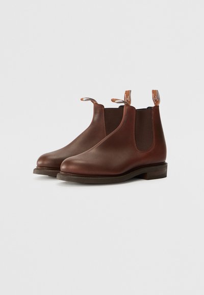 Bottes Chelsea en cuir marron avec des panneaux latéraux élastiques, des semelles plates et des languettes au niveau des talons. Texture lisse et design à bout rond.