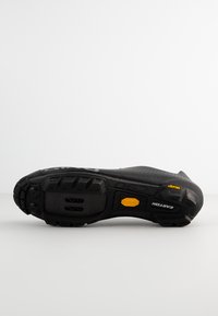 Suela de zapato negra con una textura rugosa, que presenta un prominente logo de Vibram y un patrón de tread distintivo para agarre y durabilidad.