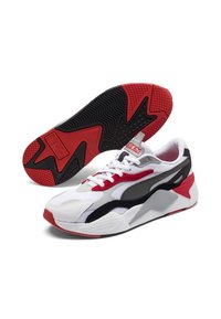 Chaussure de sport blanche avec accents rouges et noirs, dessus en mesh et synthétique, semelle texturée, et design incurvé distinctif.