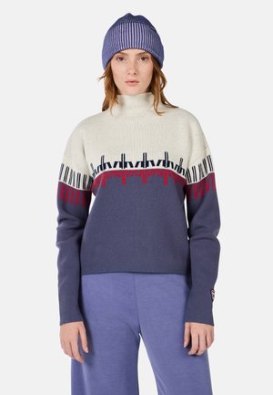 Knit sweater with a high neck; cream top, navy bottom, red and black geometric patterns. Paired with a blue striped beanie.