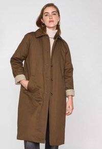 Cappotto marrone con collo a camicia, due tasche laterali e una fodera a scacchi visibile ai polsini. Realizzato in tessuto liscio con una linea dritta.