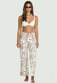 White bikini top pairs with light floral-patterned pants featuring red flower designs, wide leg fit, and front button closure. Texture is smooth.