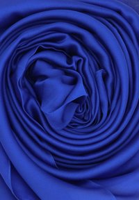 Tessuto di raso blu royal arrotolato in una spirale, che mostra una texture liscia e lucida con morbide pieghe e senza motivi o elementi visibili.