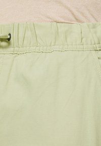 Light green shorts made of textured fabric with an elastic waistband and drawstring. Visible stitching detail along the seams.