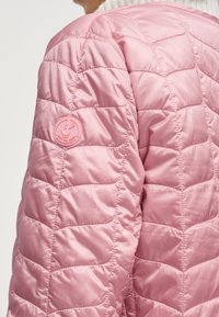 Ροζ μπουφάν με καπιτονέ υφή και μικρό κυκλικό σχέδιο με παπί και το κείμενο "Save the Duck" στο πάνω μέρος του μπράτσου.