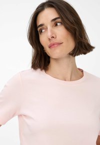 T-shirt a maniche corte rosa chiaro realizzato in un tessuto morbido e liscio, con scollatura rotonda. Presenta cuciture minime e una silhouette aderente.