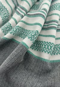 Textiel met een geweven patroon van groene en grijze strepen op een lichte achtergrond, dat contrasterende texturen en gedetailleerde geometrische ontwerpen toont.