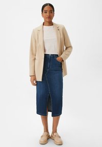 Beige blazer over a striped white and light pink top, paired with a dark blue denim pencil skirt with a front slit and cream clogs.