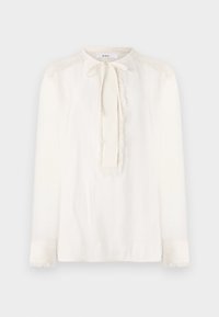 Hvit bluse med rund krage, knyttet detalj ved halsen og lange ermer. Har teksturerte frynse detaljer langs skuldrene og ermene.