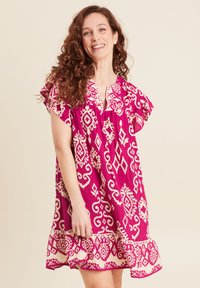 Rosenfarbendes Kleid mit kurzen, flatternden Ärmeln, das ein weißes abstraktes Design aufweist. Der Saum hat eine geraffte Kante. Weicher Stoff.
