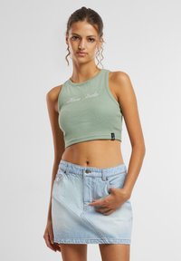 Top court vert clair à texture côtelée avec broderie "Kani Studio" ; associé à une jupe en denim bleu délavé taille haute.