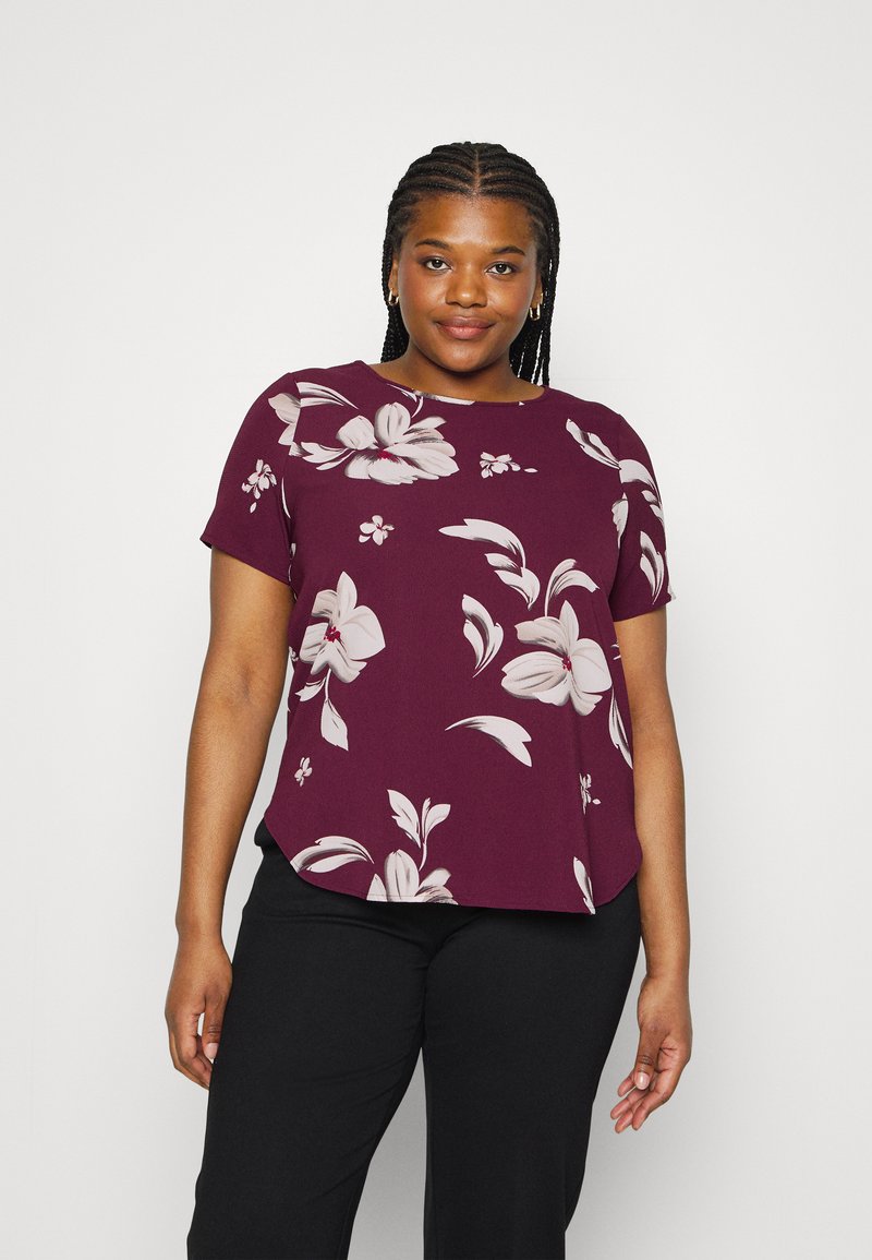 Top corto bordeaux a maniche corte con motivo floreale bianco, scollatura rotonda e orlo leggermente curvo. Tessuto morbido con una vestibilità rilassata.