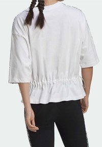 Vit bomullstop med lös passform, elastiskt snöre i midjan och korta ärmar. Har svarta detaljer längs axlarna och sidorna.