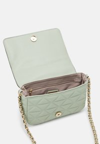 Pikowana torebka w kolorze miętowym z złotymi elementami, łańcuszkowym paskiem i zapięciem na zatrzask. Wnętrze zawiera kieszeń na zamek błyskawiczny oraz beżową podszewkę.