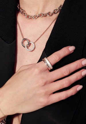 Smycken i roséguld av metall som inkluderar ett länkade kedjehalsband, en dubbelringpendant med en ring som är inlagd med klara stenar, samt en matchande ring.