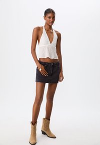 Witte haltertop met een diepe V-hals en textuurstof, gecombineerd met een zwarte denim minirok en tan cowgirl laarzen.