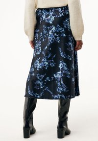 Larga falda negra con un patrón floral en tonos azules y morados, hecha de un material suave con un ligero brillo. A la altura de la rodilla con un corte holgado.