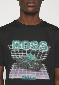 Black short-sleeve t-shirt featuring a graphic of a motorcycle with turquoise accents, "BOSS" text above and "ENTER" text below on a grid pattern.